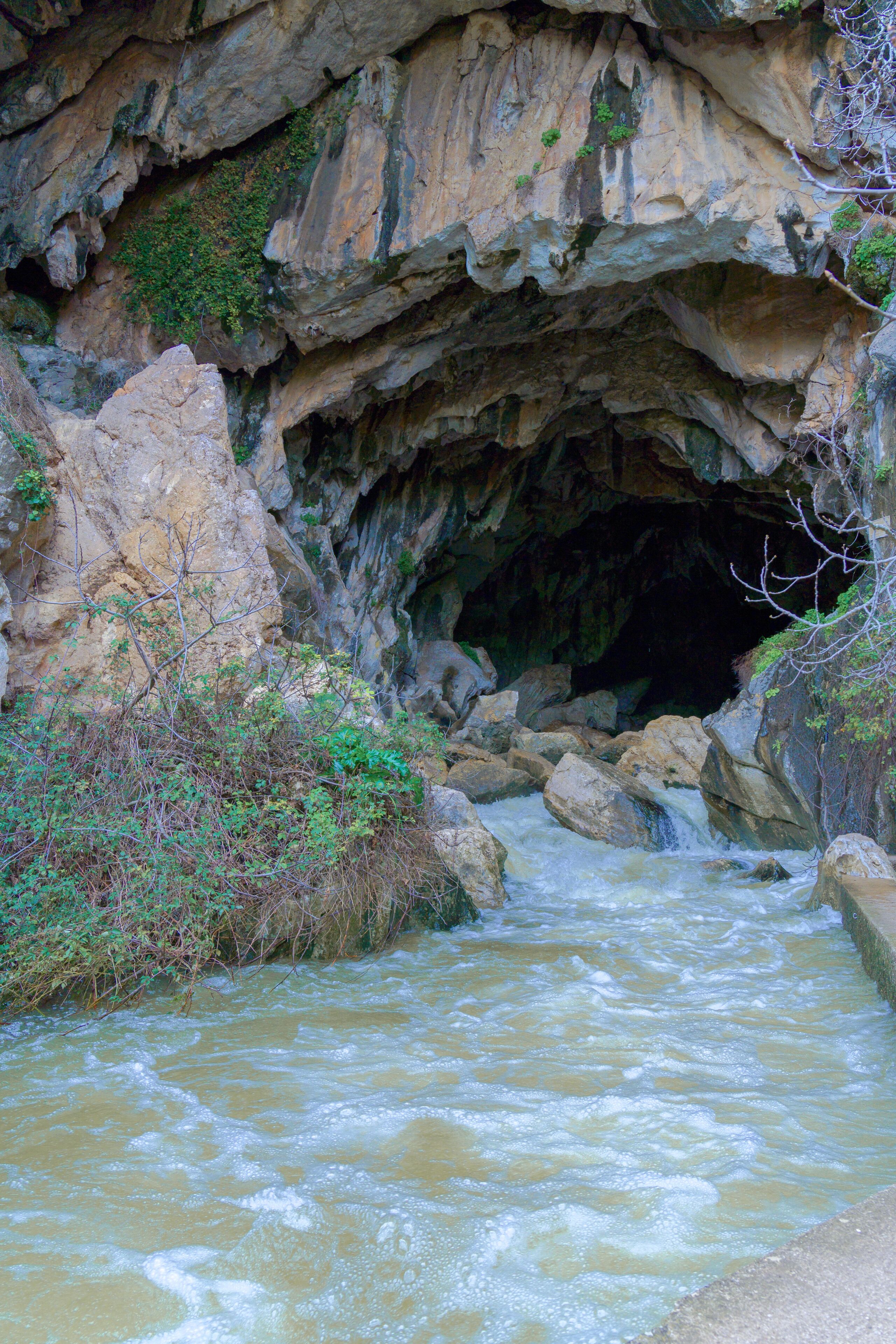 deep cave in the mountain from which a river with a waterfall flows out.