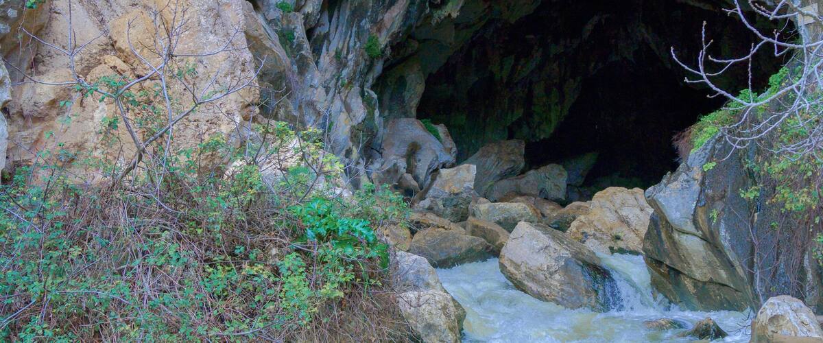 deep cave in the mountain from which a river with a waterfall flows out.