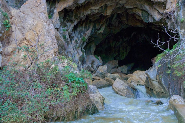 deep cave in the mountain from which a river with a waterfall flows out.