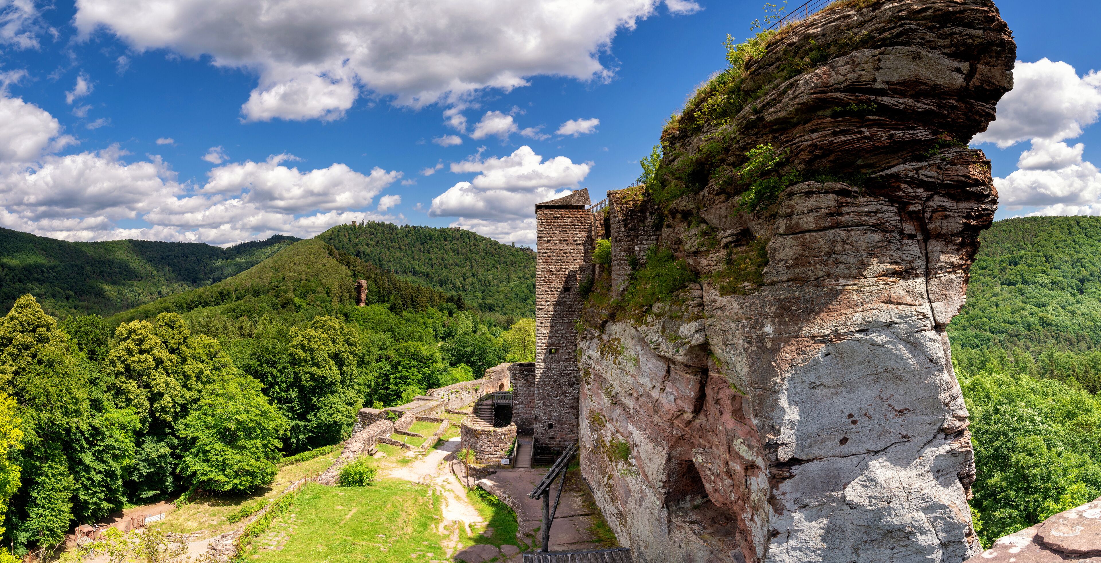 A historical stone structure with ruins, set against a backdrop of lush green hills and a clear blue sky.