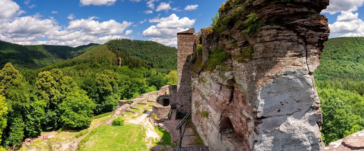 A historical stone structure with ruins, set against a backdrop of lush green hills and a clear blue sky.