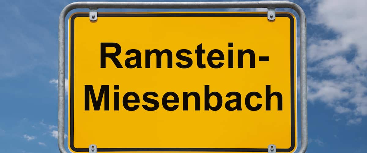 A yellow sign with the text 'Ramstein-Miesenbach' against a blue sky with clouds.