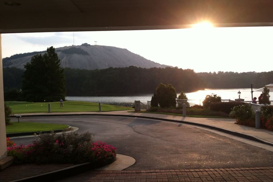 A landscaped area with a curved driveway, a body of water, and a mountain in the background.