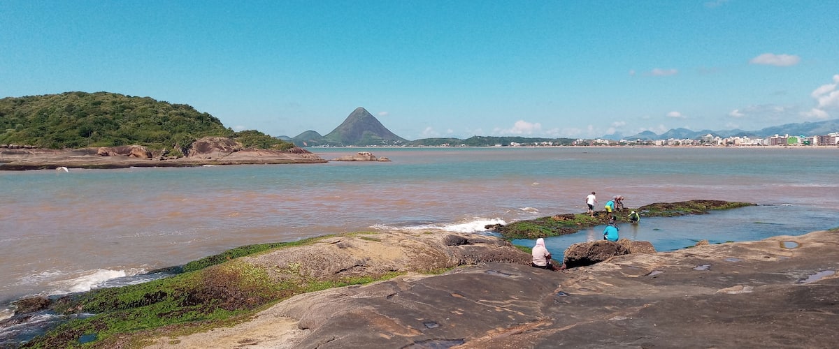 A coastal landscape with rocky shores, calm waters, and a distant mountain.