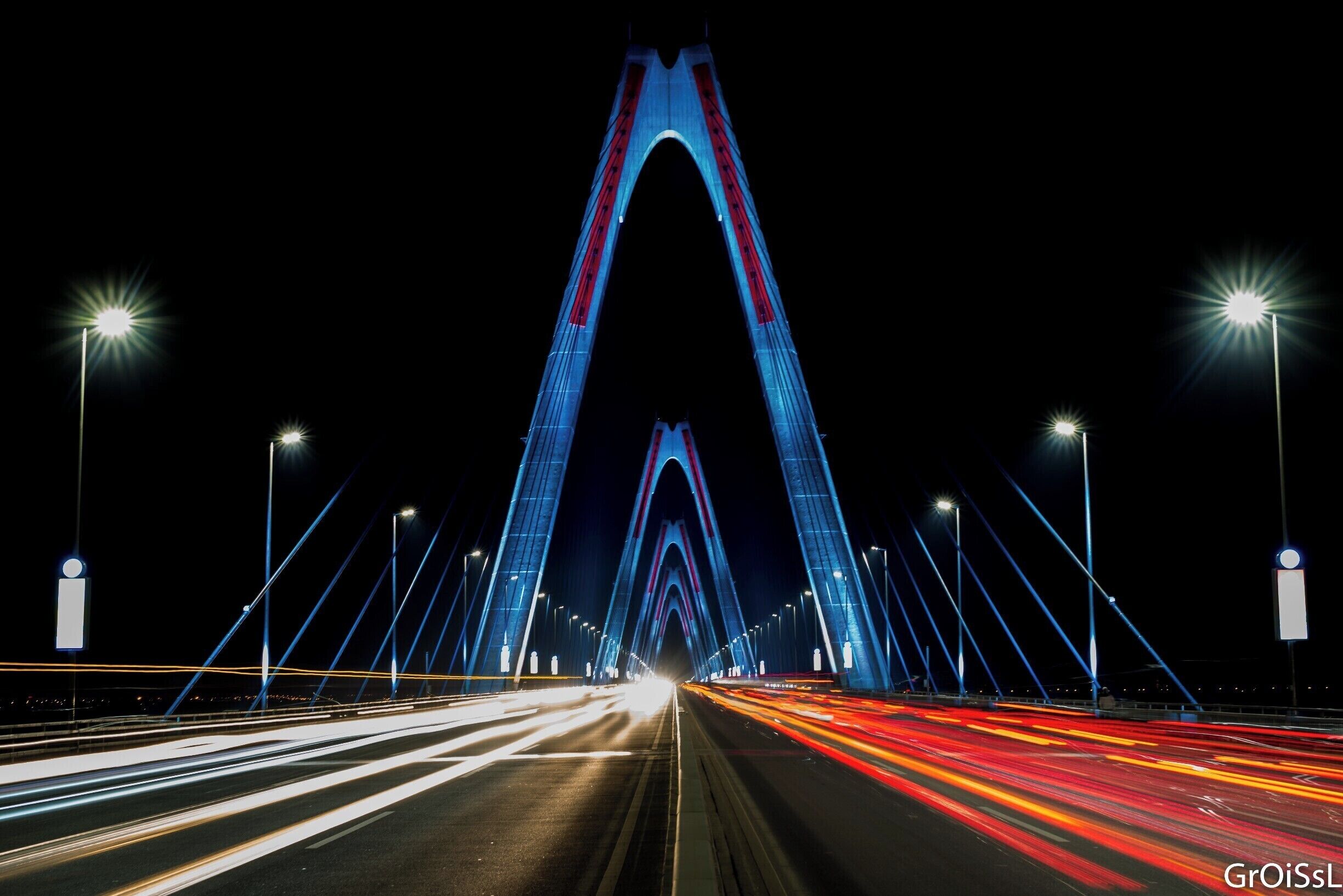 A nighttime view of a large, illuminated bridge with multiple light beams converging towards the center.