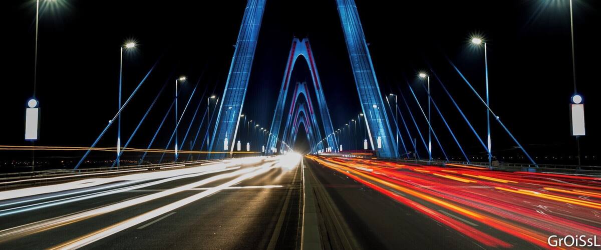 A nighttime view of a large, illuminated bridge with multiple light beams converging towards the center.