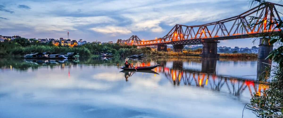 A calm river with a boat, a bridge, and a cityscape in the background.