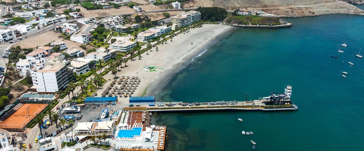 An aerial view of a coastal town with a beach, a pier, and a mountain in the background.