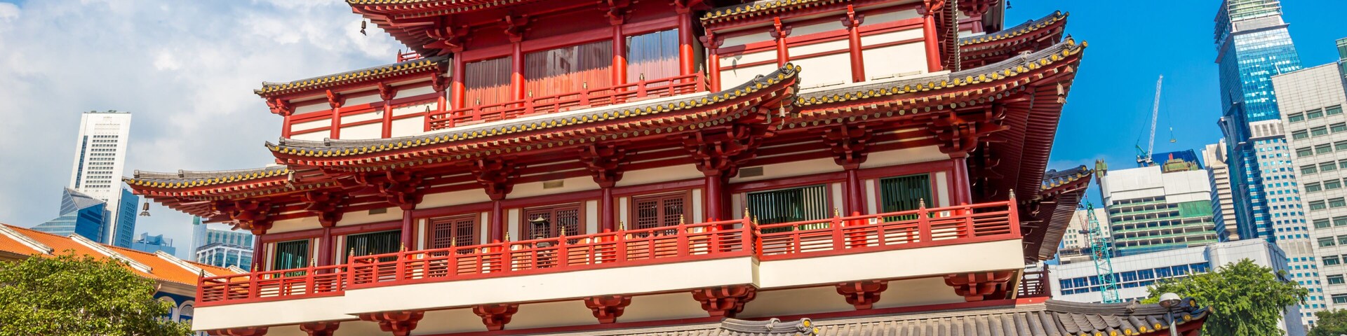 Un edificio tradicional de varios niveles con colores rojo y blanco, rodeado de rascacielos modernos.