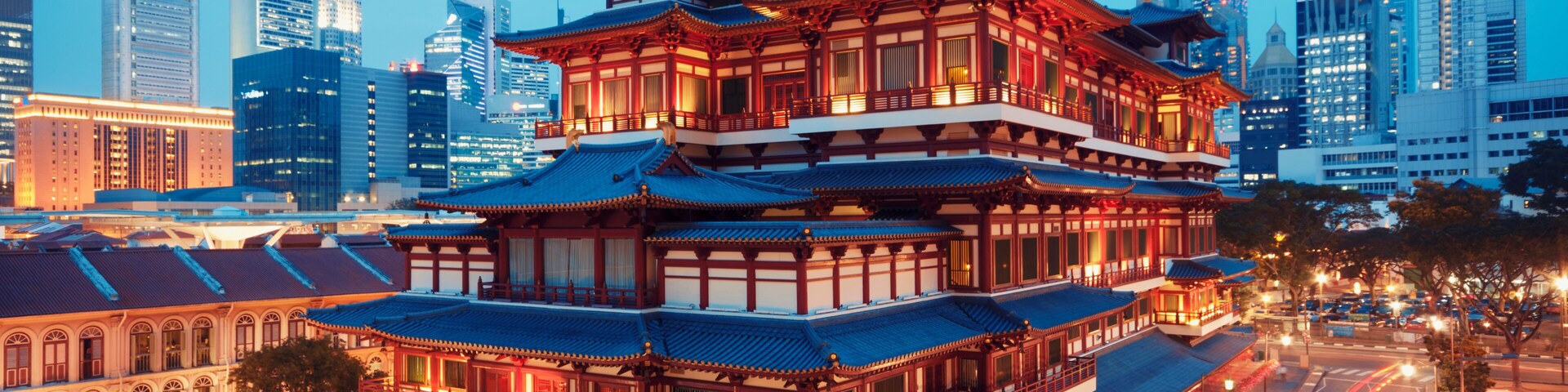 Un edificio tradicional de varios niveles con arquitectura ornamentada, rodeado por un paisaje urbano moderno con rascacielos.
