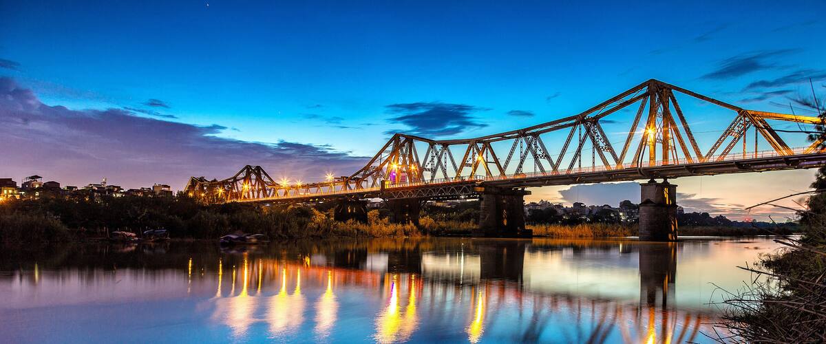 A bridge at dusk with its lights reflecting on the water.