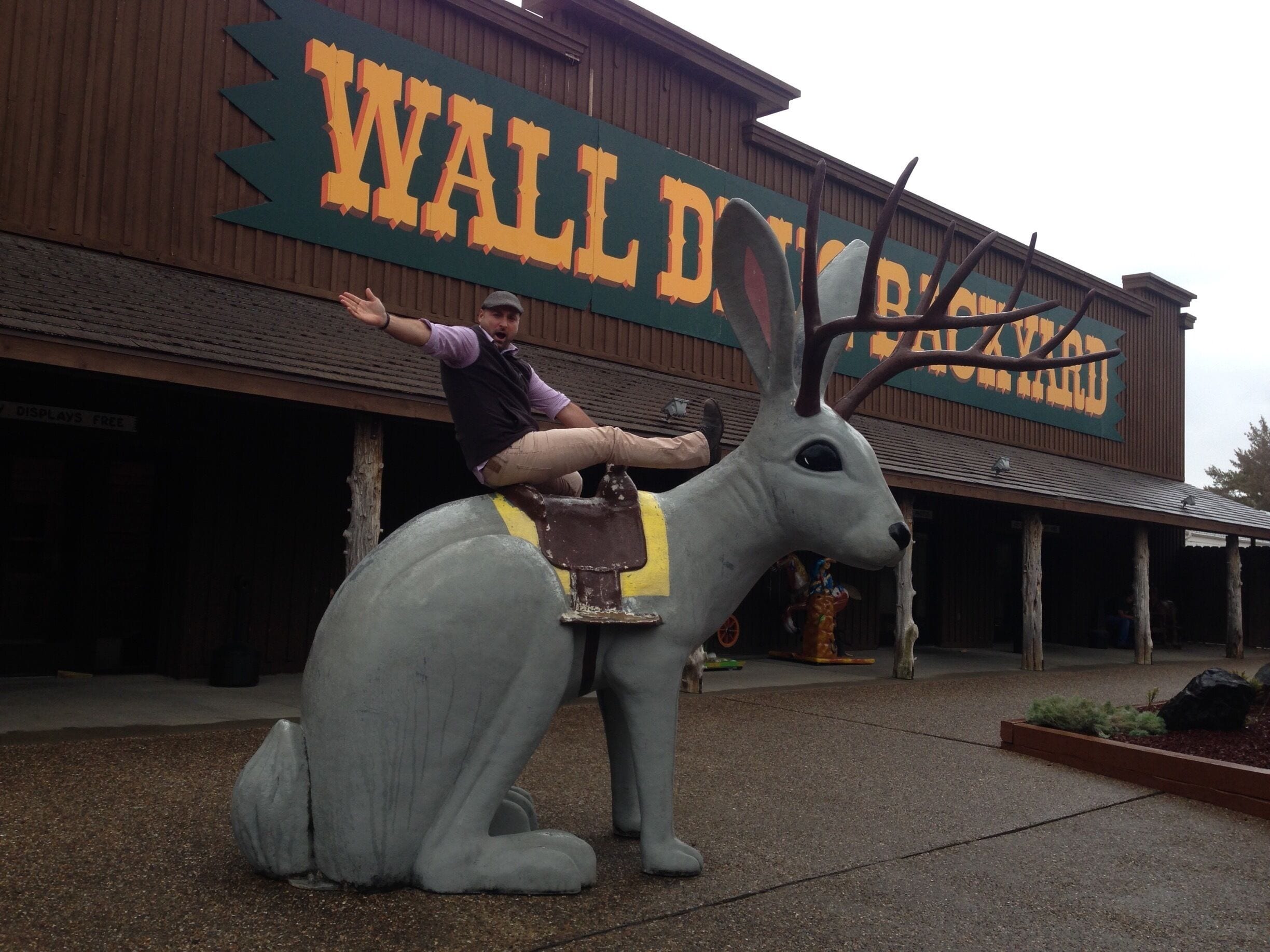 A man sitting on a large deer statue in front of a building with a sign reading "WALLDOPE".