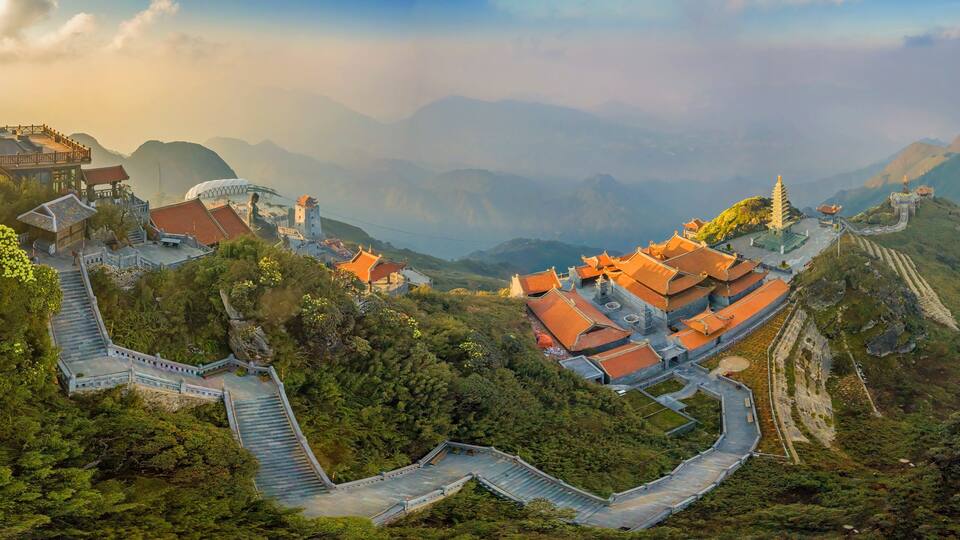A mountainous temple complex with traditional architecture, terraced pathways, and a winding road.