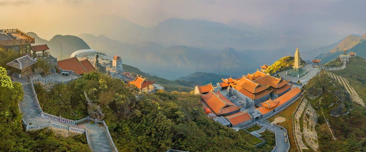 A mountainous temple complex with traditional architecture, terraced pathways, and a winding road.