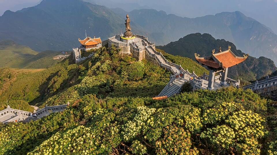 A temple complex on a mountain with traditional architecture and a statue.