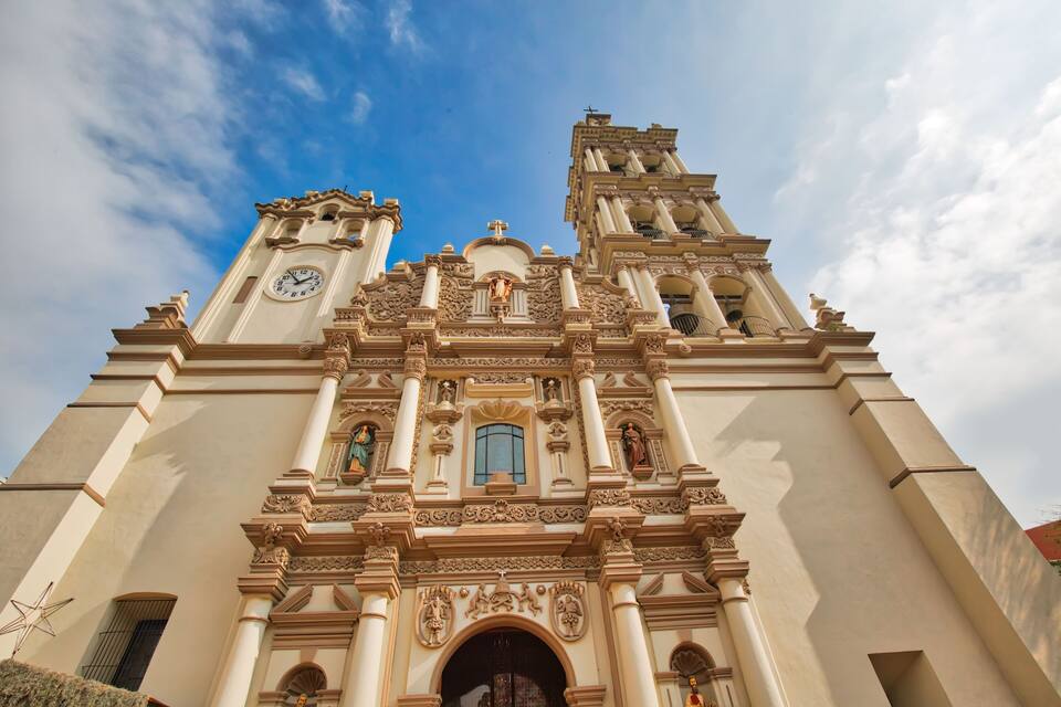 Una església històrica d'arquitectura ornamentada, amb una torre del rellotge i un cel blau clar.