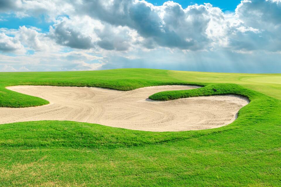 A golf course with sand bunkers and a clear blue sky.