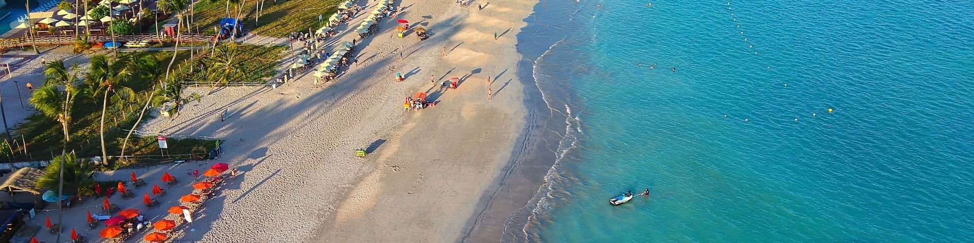 A beach with umbrellas, palm trees, and boats.