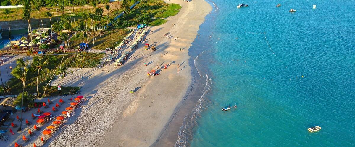 A beach with umbrellas, palm trees, and boats.