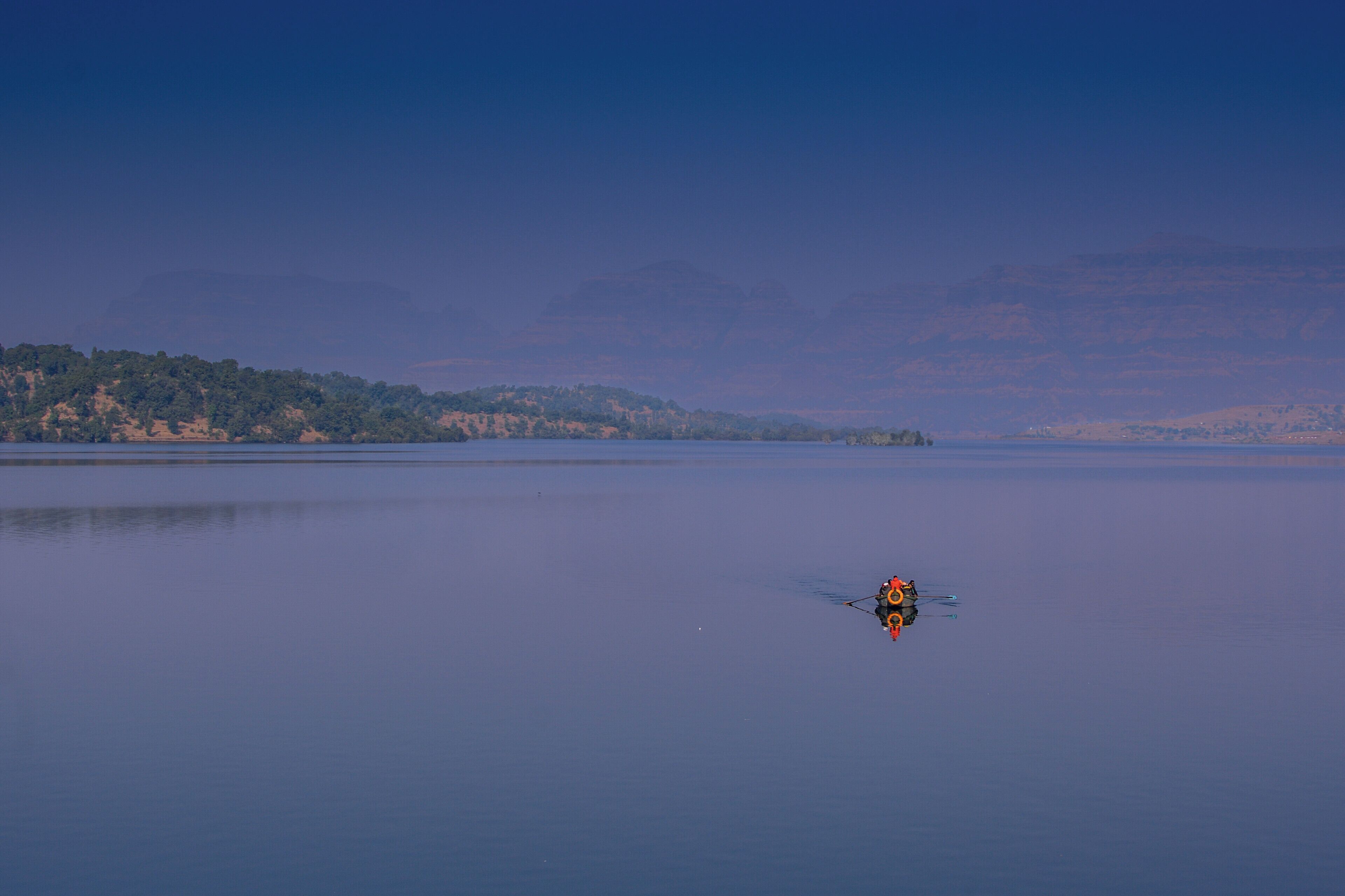 A calm lake with a small boat in the center and a forested hill in the background.