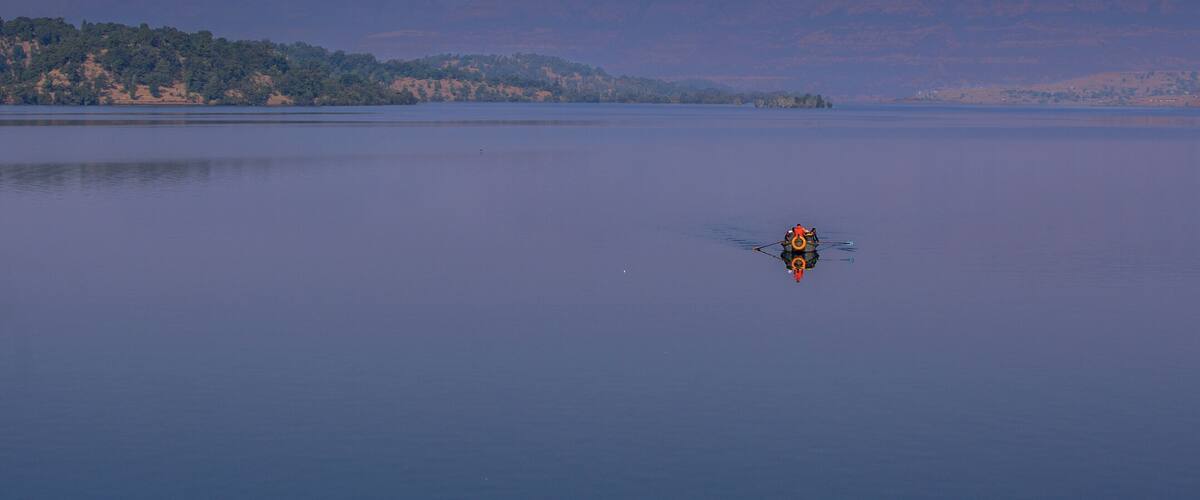 A calm lake with a small boat in the center and a forested hill in the background.