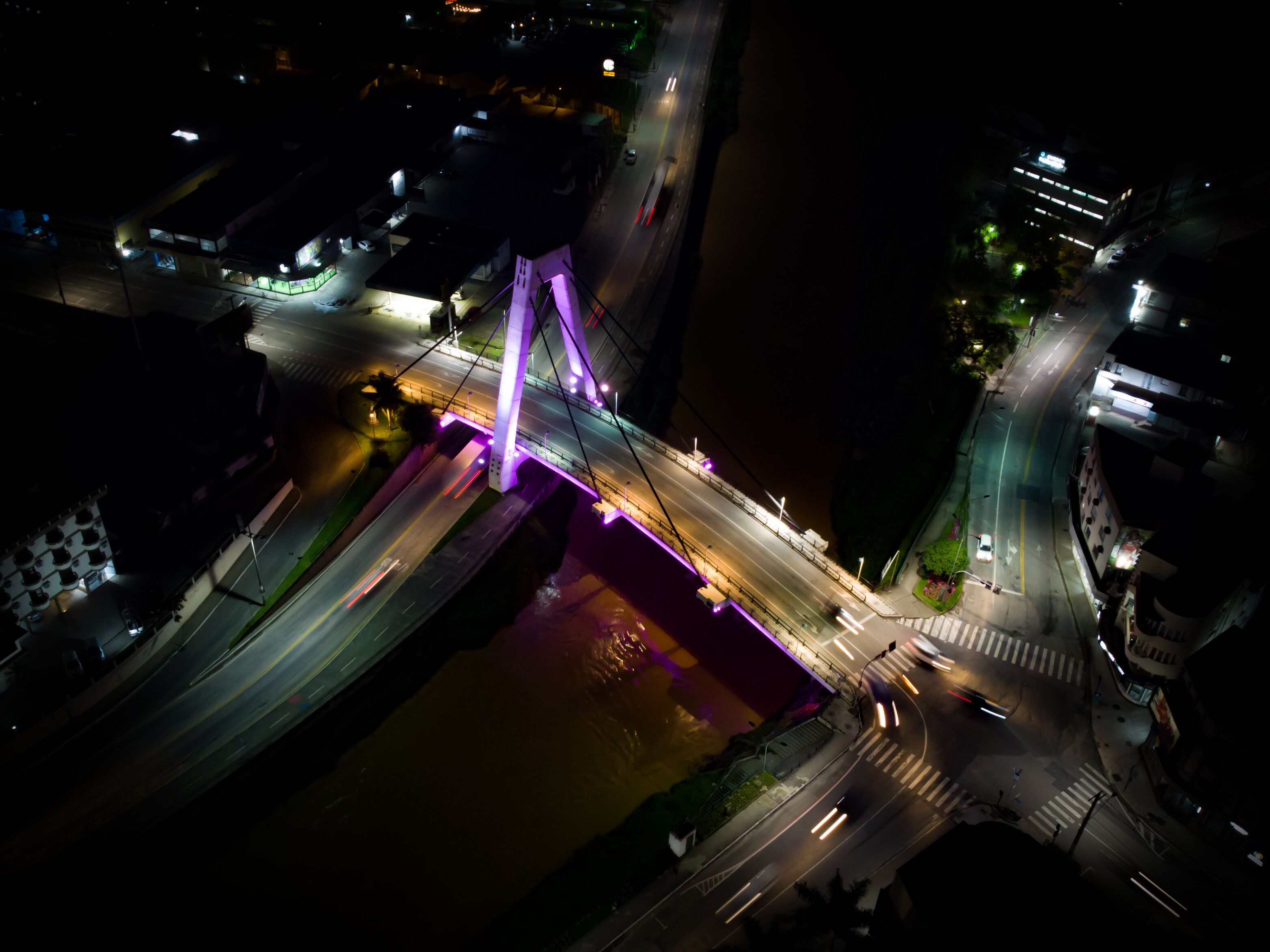 An aerial view of a bridge with purple lighting, surrounded by urban infrastructure.