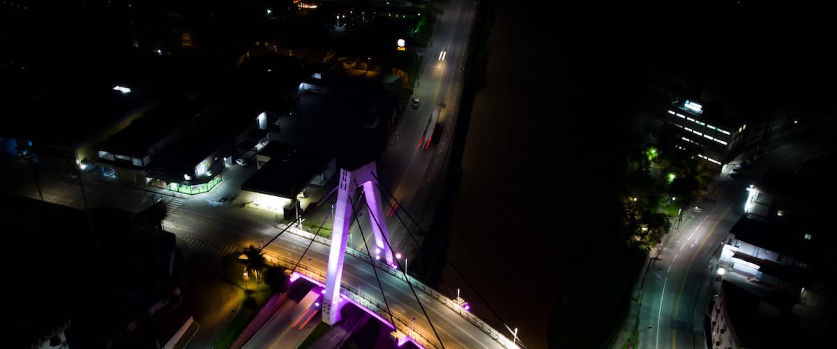 An aerial view of a bridge with purple lighting, surrounded by urban infrastructure.