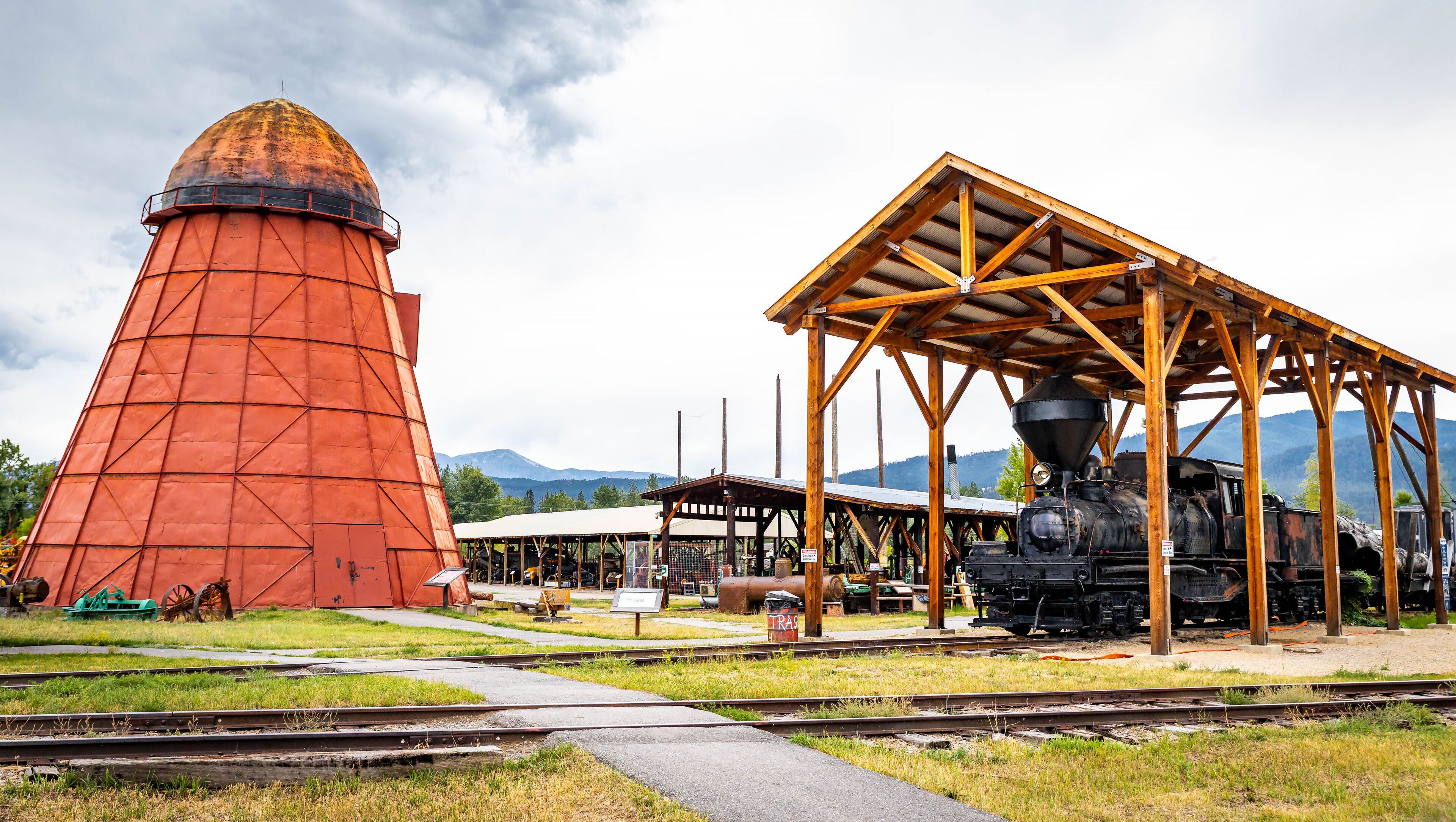 A red silo, a wooden train shed, and a steam locomotive at a railway station.