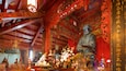 An ornate temple interior with golden statues, red decorations, and floral arrangements.