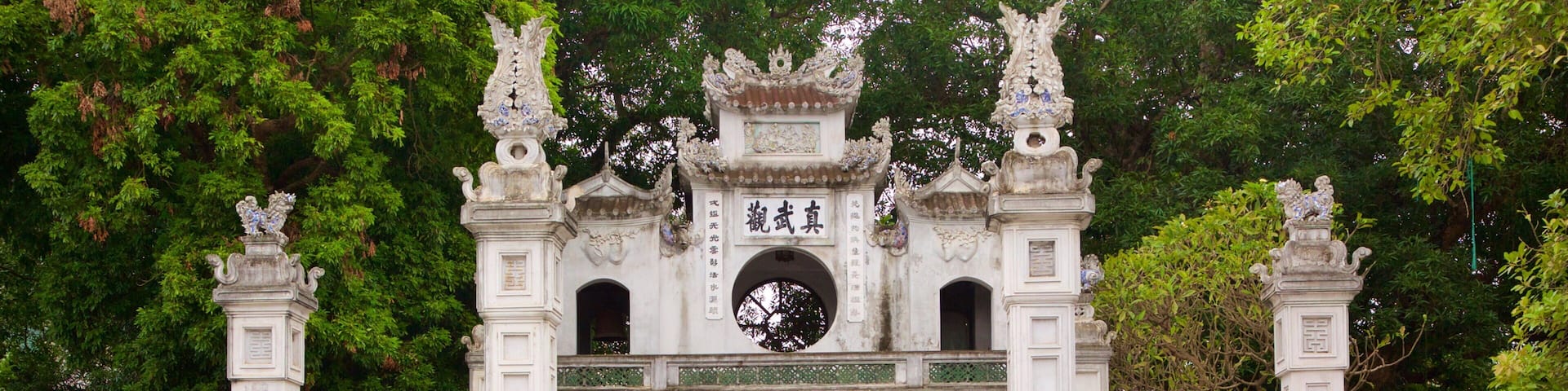 A historic gate with ornate carvings and inscriptions, surrounded by lush greenery.