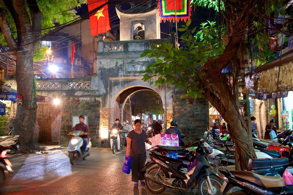 A bustling street scene with a traditional archway, motorcycles, and various shops.