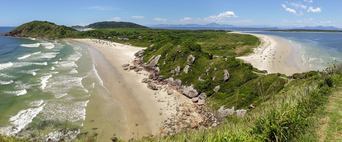 A coastal landscape with a sandy beach, rocky outcrops, and a green hill in the distance.