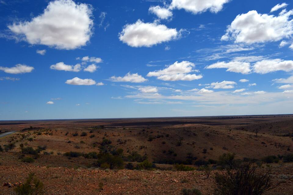 Eine weite, trockene Landschaft mit vereinzelter Vegetation unter blauem Himmel mit vereinzelten Wolken.
