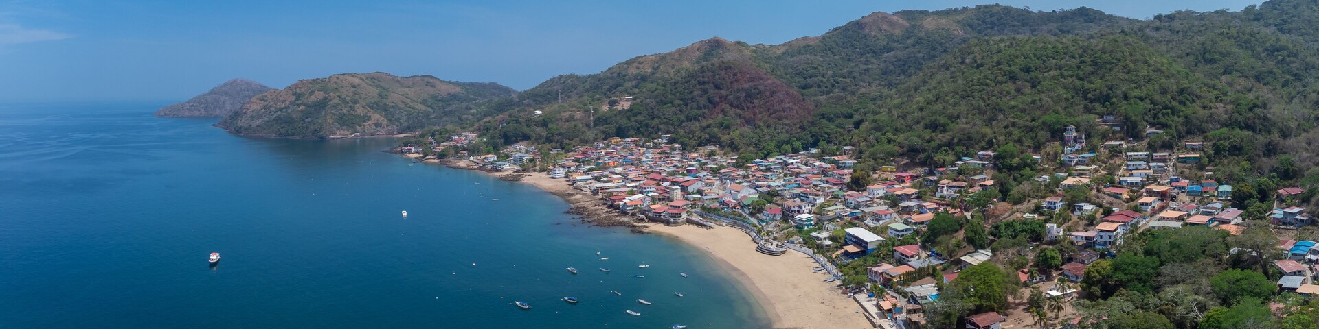 A coastal town with a beach, boats, and mountainous terrain.