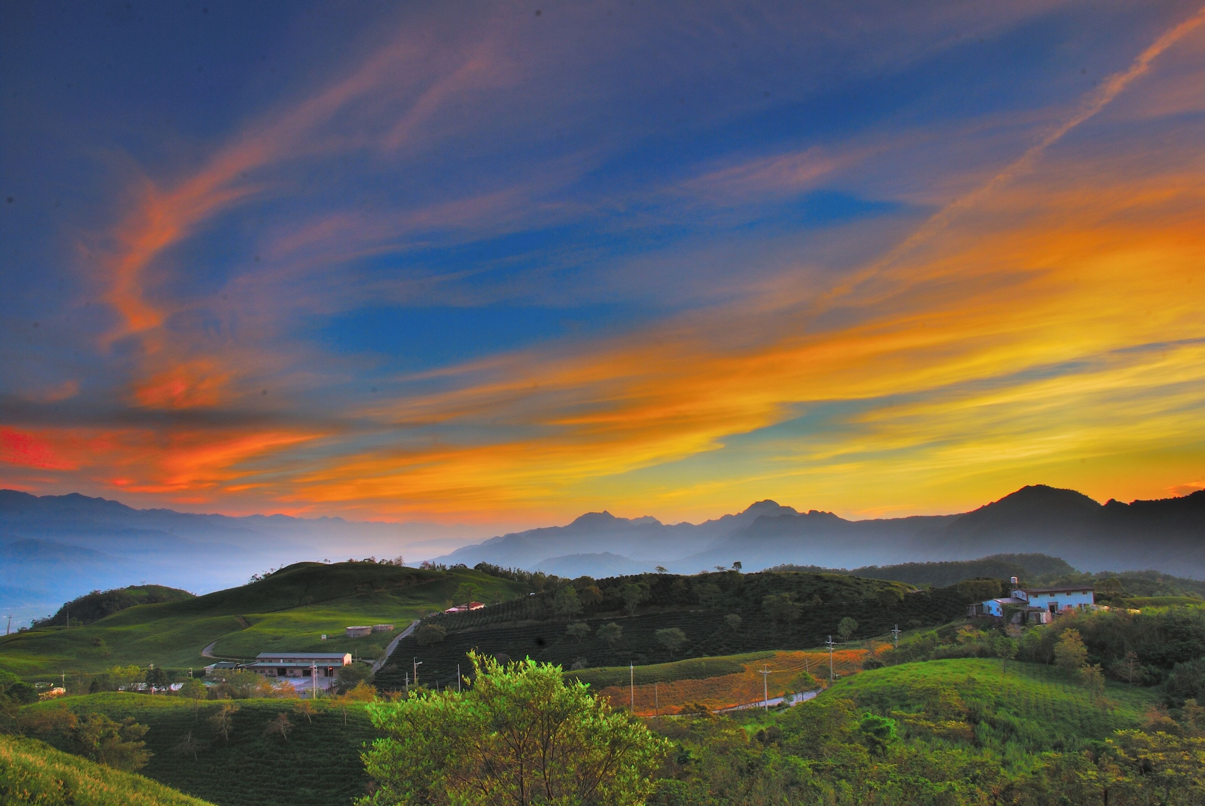 A landscape with rolling hills, a small house, and a distant mountain range under a colorful sky.