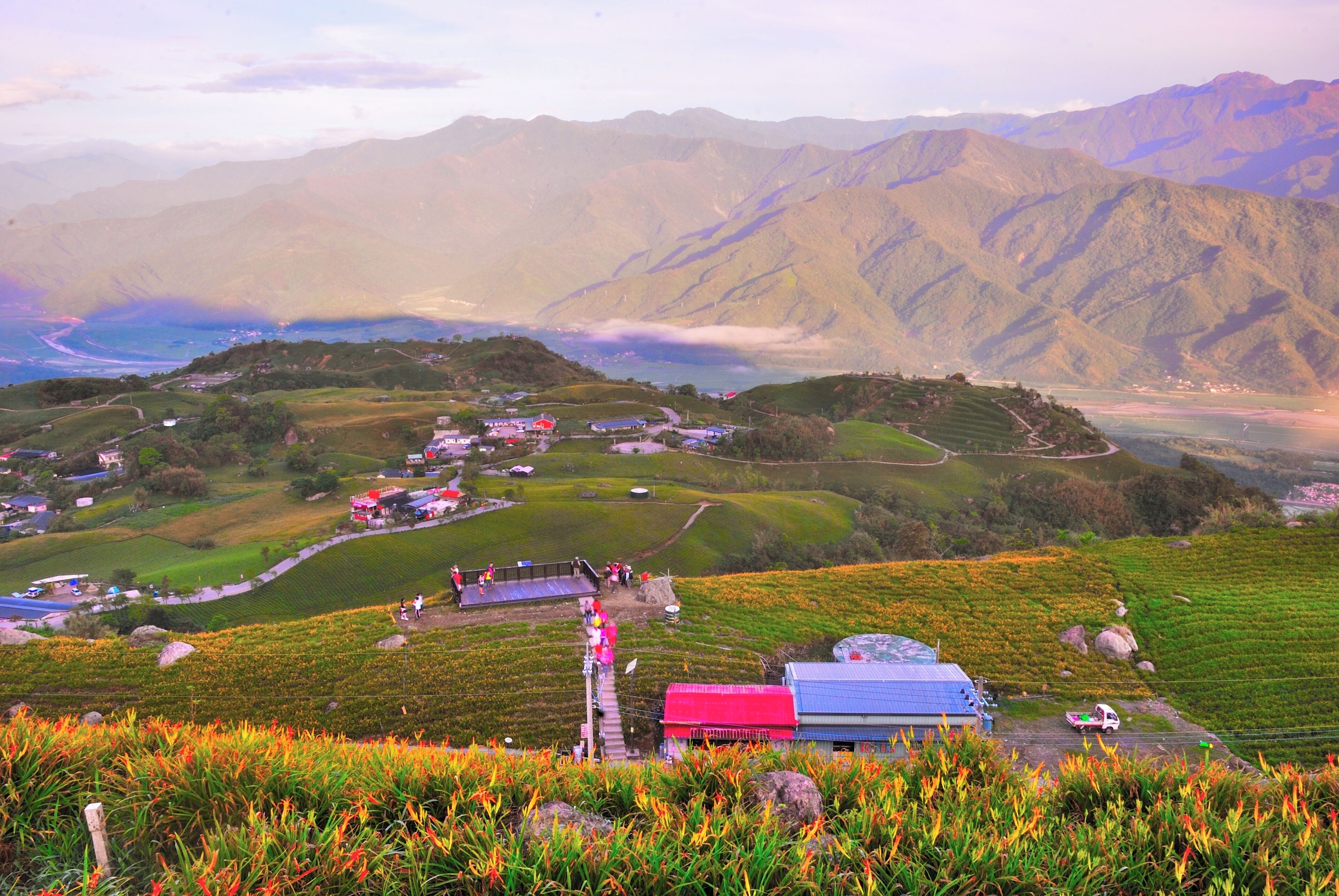 A mountainous landscape with terraced fields, a small settlement, and a body of water in the distance.