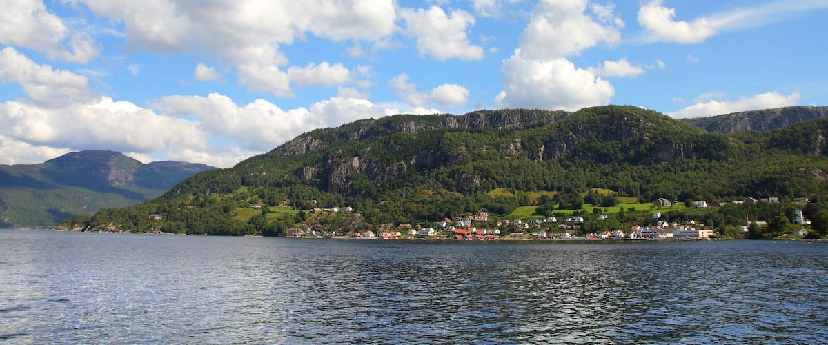 A lake with a village on a green hillside, surrounded by mountains.