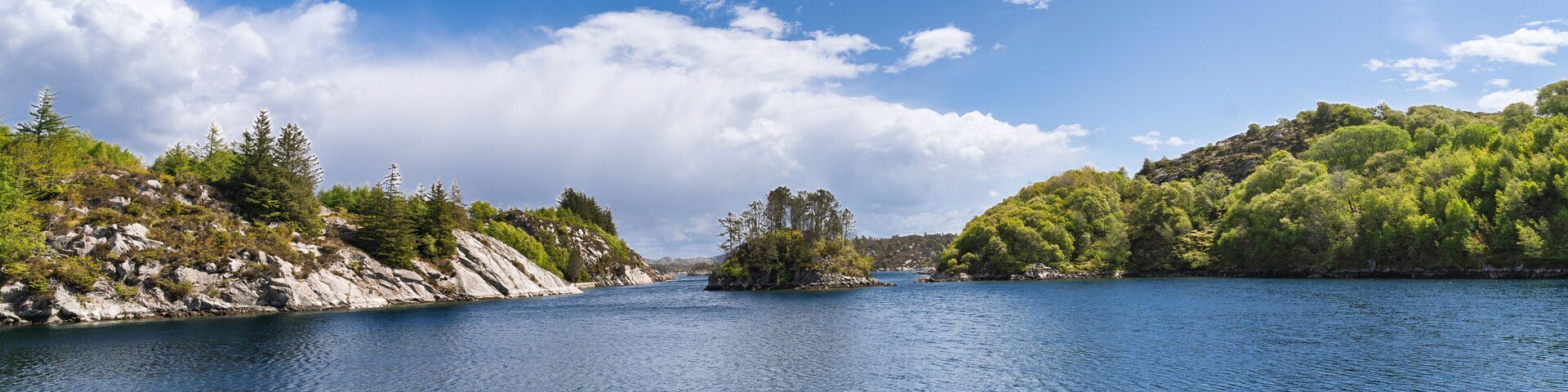 A calm lake surrounded by rocky cliffs and dense greenery.