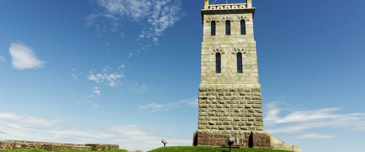 A stone tower with a flag on top, set against a clear blue sky.