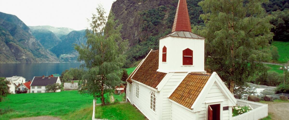 A white church with a red steeple surrounded by green fields and mountains.