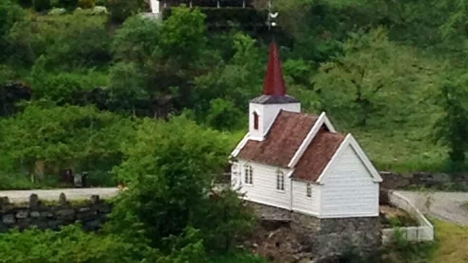 En vit kyrka med ett rött torn på en grönskande sluttning.