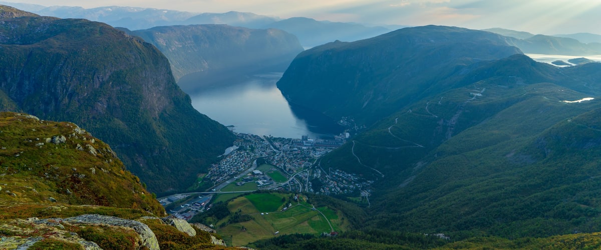 A valley with a lake surrounded by mountains, a town in the valley, and a winding road.