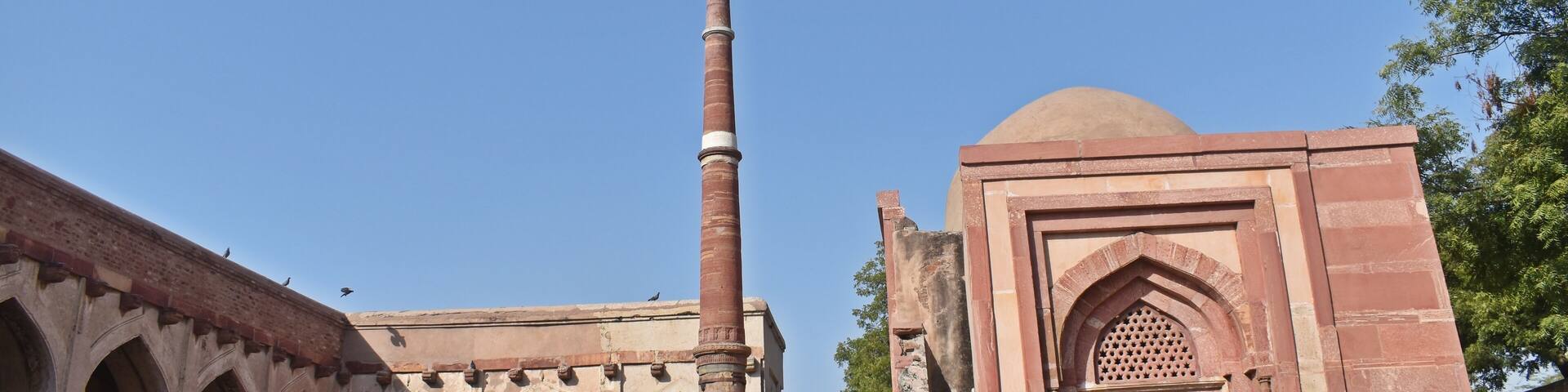 An ancient building with arched corridors and a tall minaret.