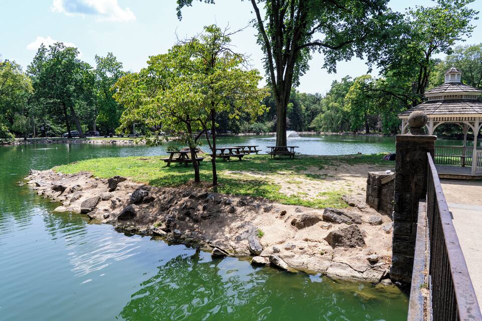 Un parc avec un étang, des tables de pique-nique, un kiosque et des arbres.