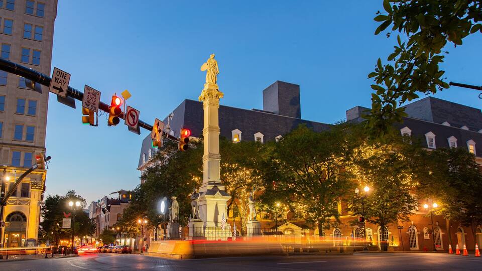 A city square with a prominent monument, traffic lights, and illuminated trees.