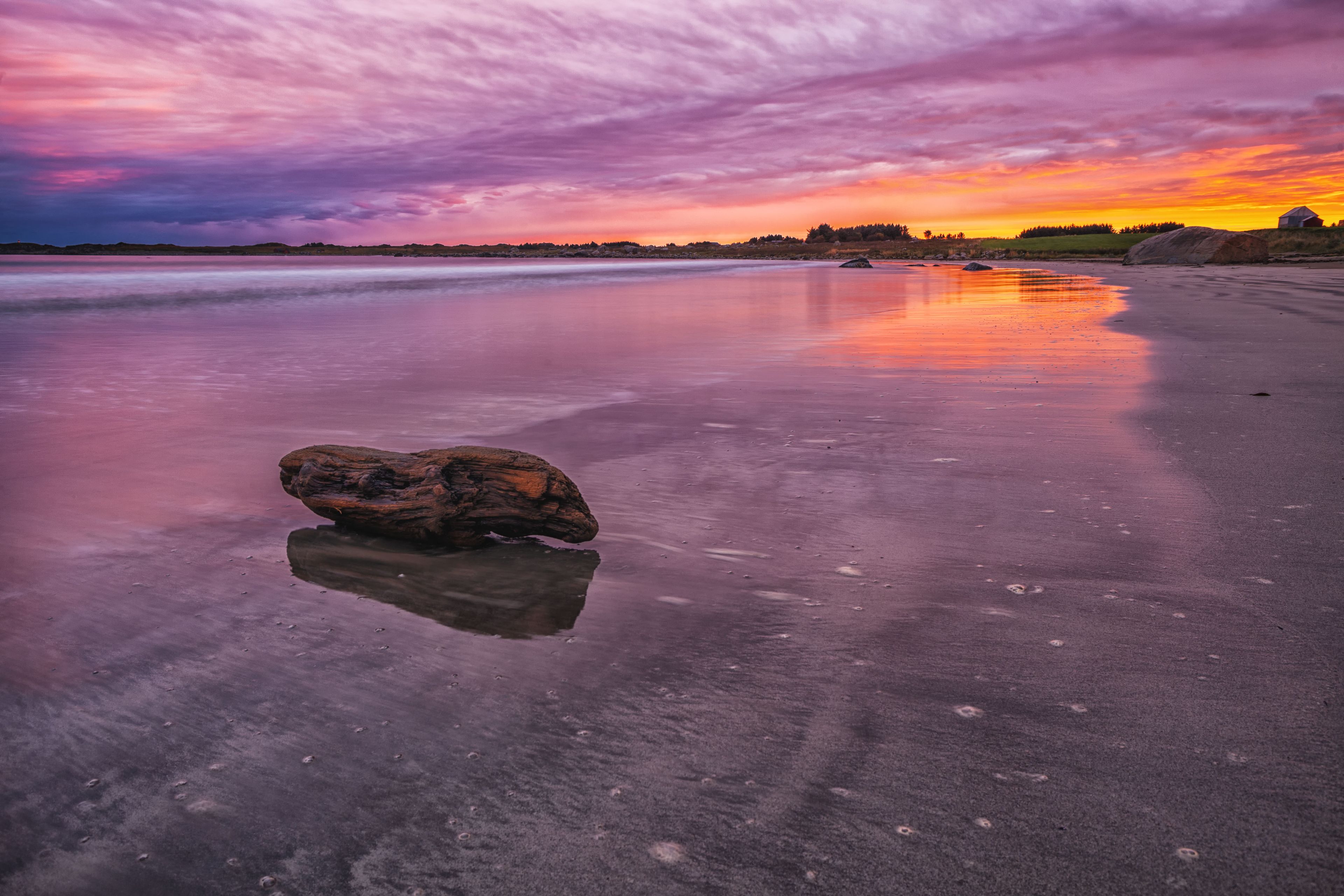 A beach with a large rock in the foreground and a sunset in the background.