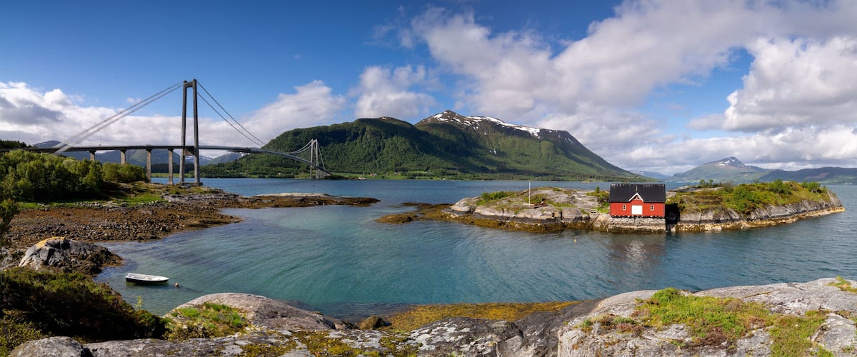 A bridge over a fjord, a red house on a small island, and mountains in the background.