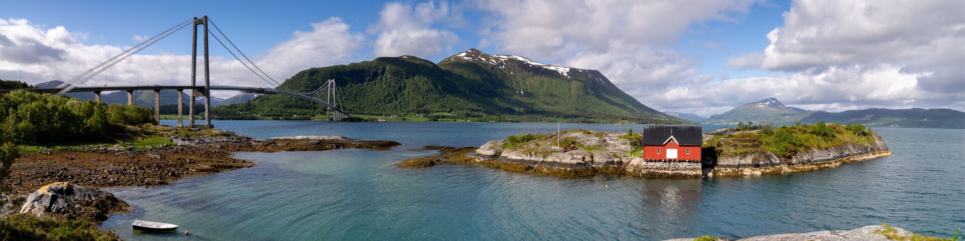 A bridge over a fjord, a red house on a small island, and mountains in the background.