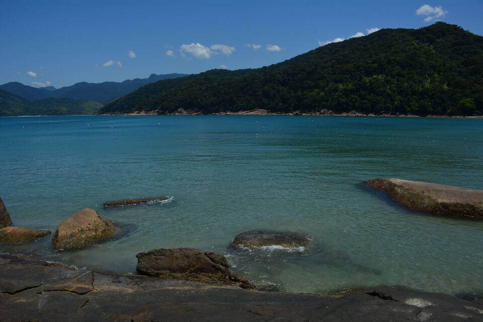 A clear turquoise lake surrounded by rocky shores and a forested mountain in the background.