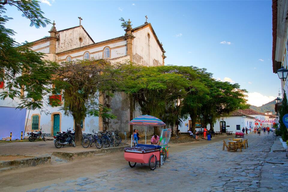 A cobblestone street lined with historic buildings, a church, and a colorful street vendor cart.
